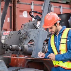 Engineer or foreman checking inventory or task details at container yard warehouse while wearing PPE and holding tablet., Logistics concept inside the shipping, import, and export industries.