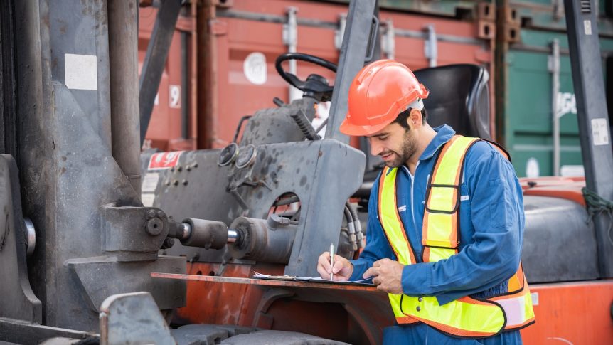 Engineer or foreman checking inventory or task details at container yard warehouse while wearing PPE and holding tablet., Logistics concept inside the shipping, import, and export industries.